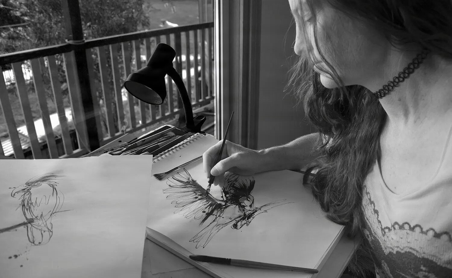 Black and white photo of artist Danielle Lattadrawing at a desk