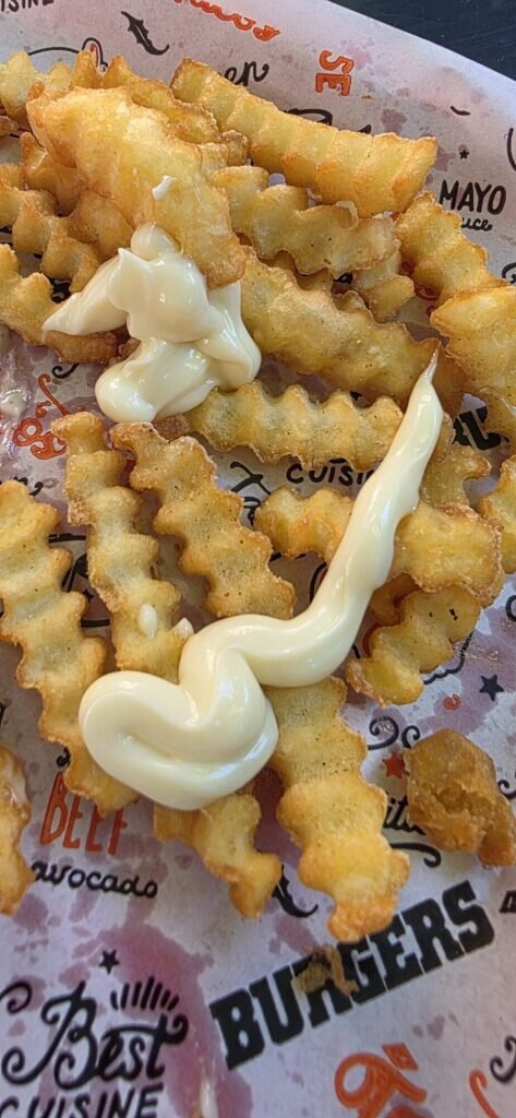 Crinkle cut chips with a swirl of mayonnaise on printed burger paper, Avignon