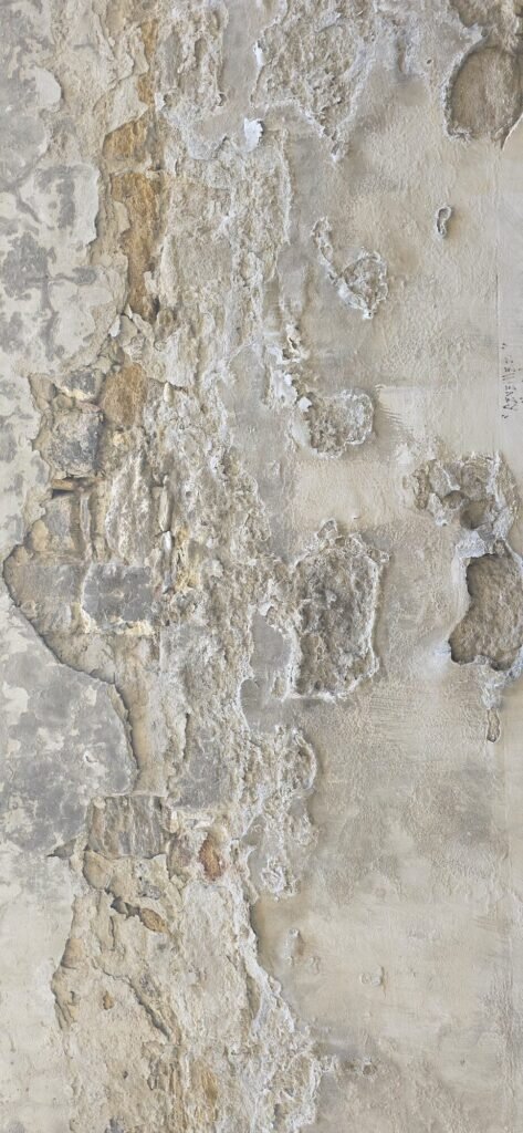 Peeling limewash on an old Avignon wall, pale render lifting off grey stone in irregular shapes
