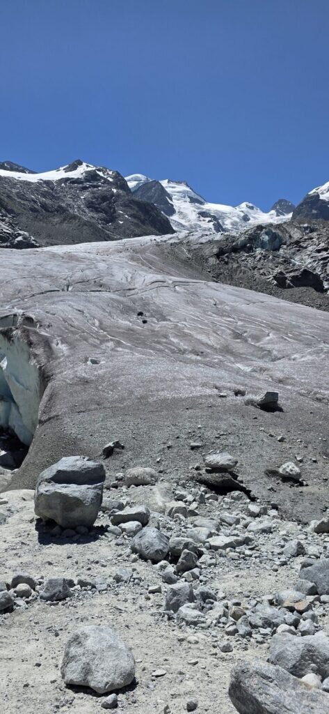 The grey debris-covered tongue of the Morteratsch glacier below snow-capped peaks
