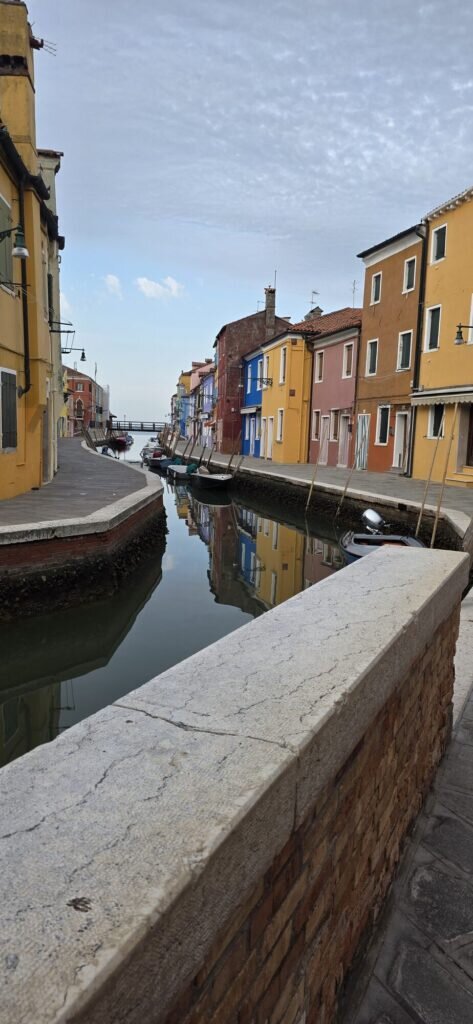 A canal on Burano lined with brightly painted houses reflected in still water