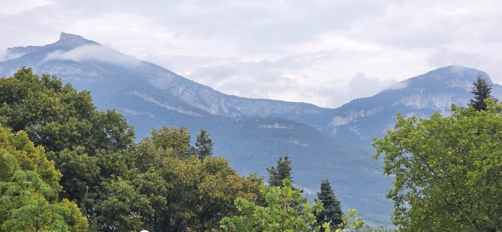 The limestone wall of the Bauges massif above Chambéry with low cloud along the ridge and trees in the foreground