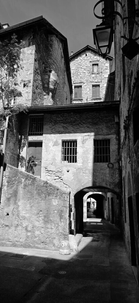 Black and white photograph of a rough stone corner in the Chambéry old town, with a low archway opening onto a narrow passage beyond
