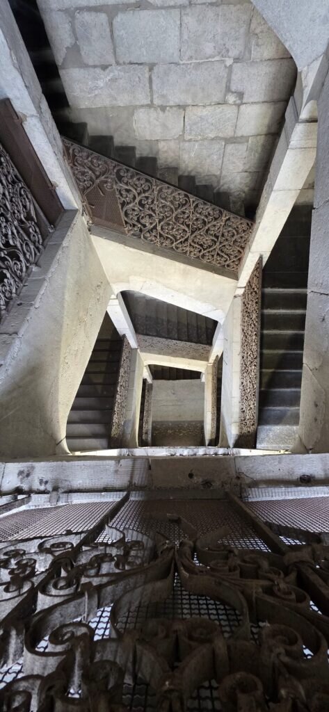 Looking straight down an old stone stairwell in Chambéry with an ornate wrought iron balustrade spiralling away flight after flight