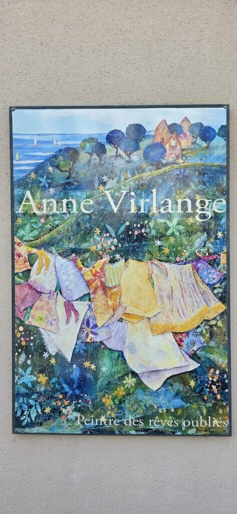 Painted exhibition panel on a wall reading Anne Virlange, peintre des reves oublies, showing washing on a line above a blue and green landscape