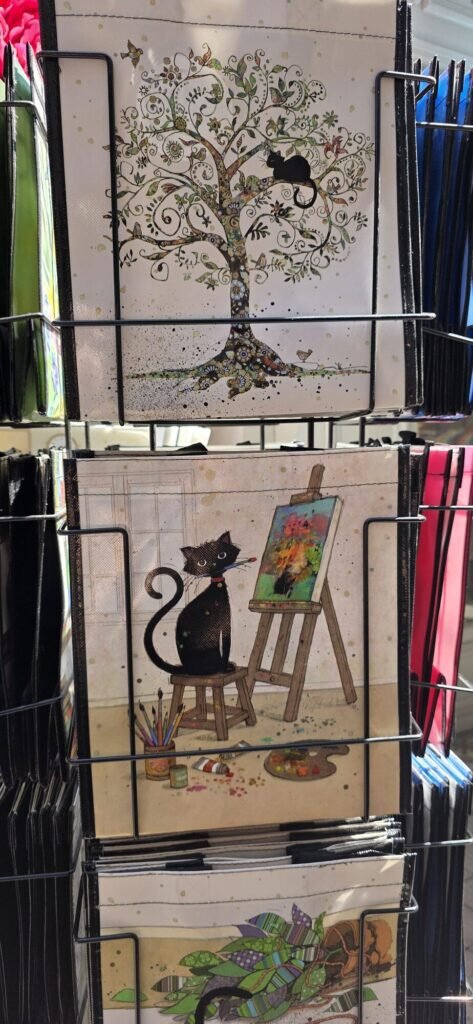 A card rack holding illustrated cards, one showing a black cat sitting on a stool at an easel with a paintbrush in its mouth