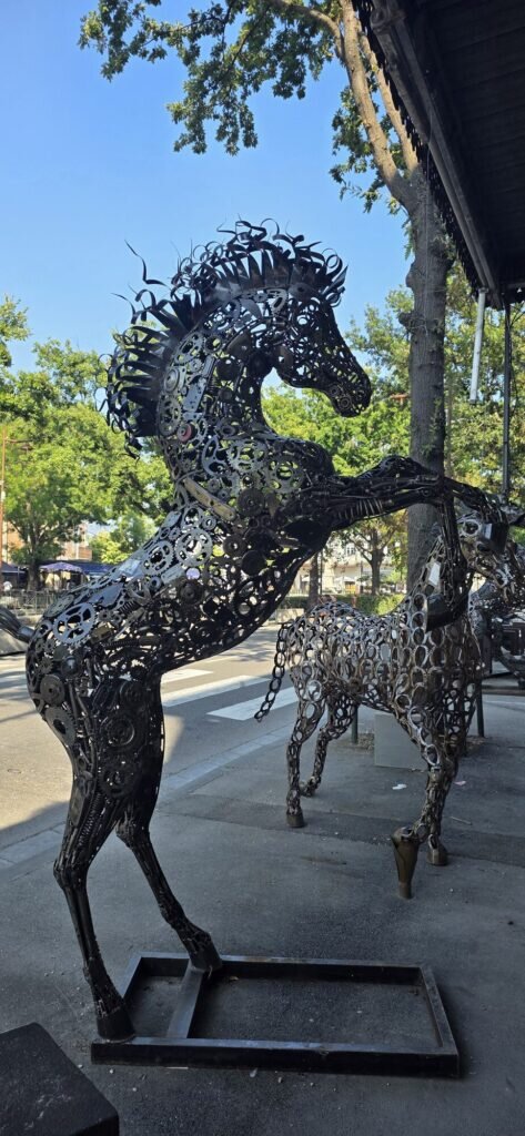 Two life size horses built from scrap gears, chains, sprockets and spanners standing under an awning at the top of avenue de la Liberation in L'Isle-sur-la-Sorgue