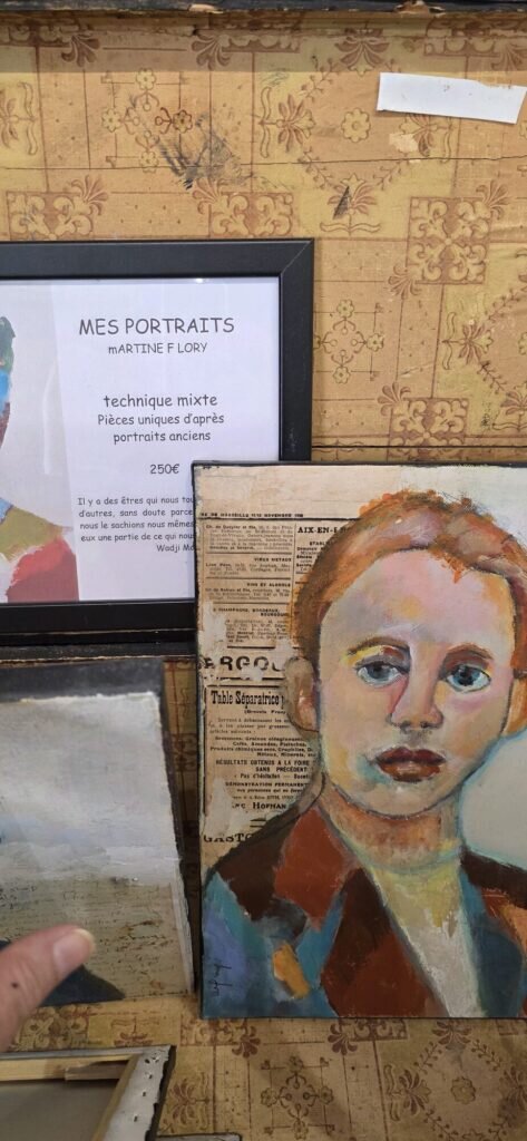 A mixed media portrait painted over old newspaper next to a framed price card reading Mes Portraits, technique mixte, 250 euros