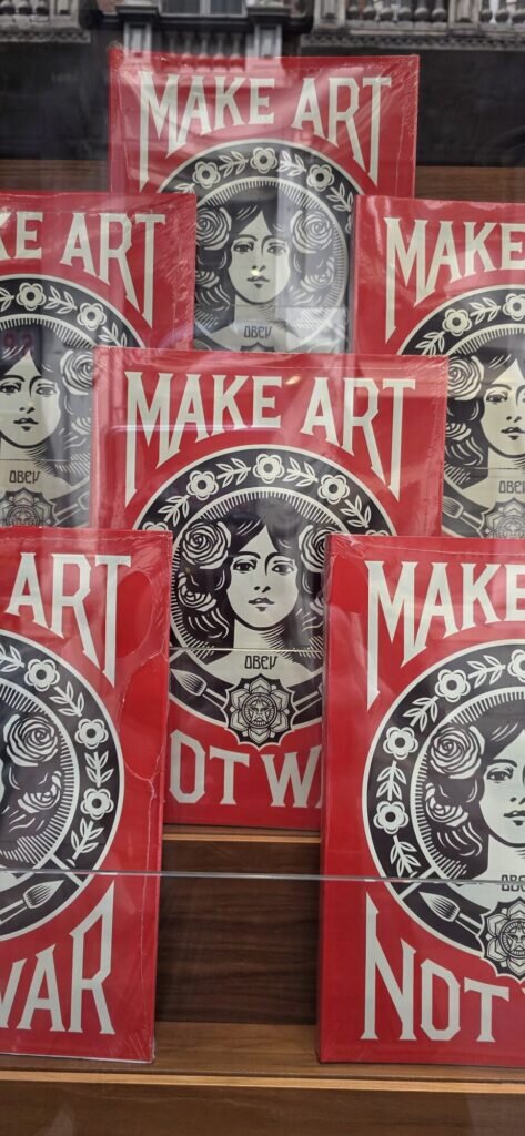 Six red and cream Shepard Fairey Make Art Not War prints stacked leaning in a row in a Turin display