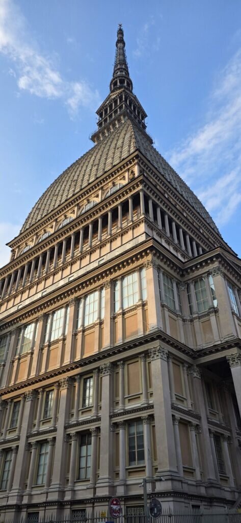 The Mole Antonelliana in Turin seen from directly below, its tiered stone body and tall spire against a morning sky