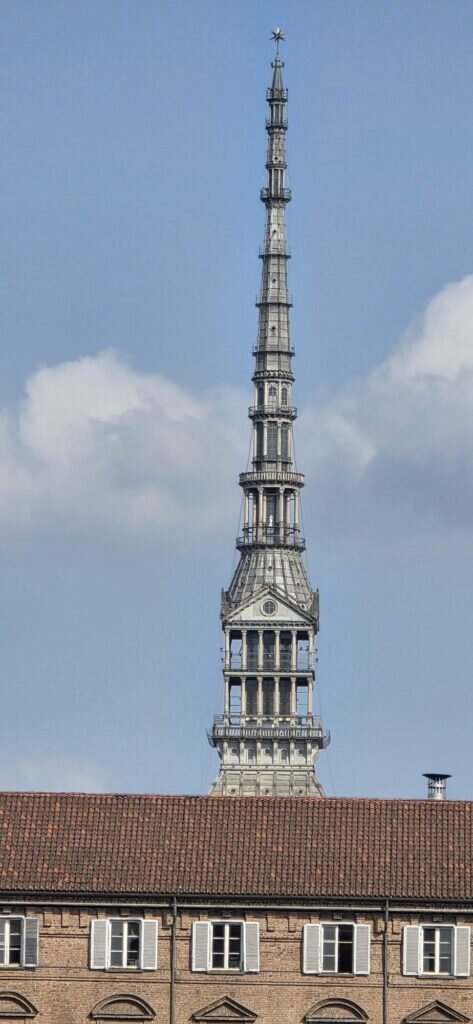 The spire of the Mole Antonelliana rising above ochre Turin rooftops against a soft afternoon sky