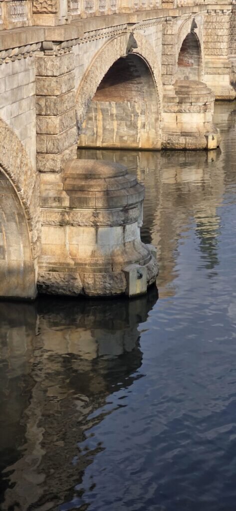 A stone bridge over the calm River Po in Turin, its arches reflected in the still water with green hills behind