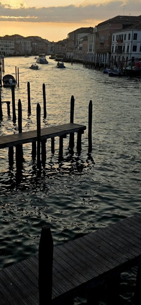 A quiet Venetian canal at first light with wooden mooring poles and boats against a golden sky