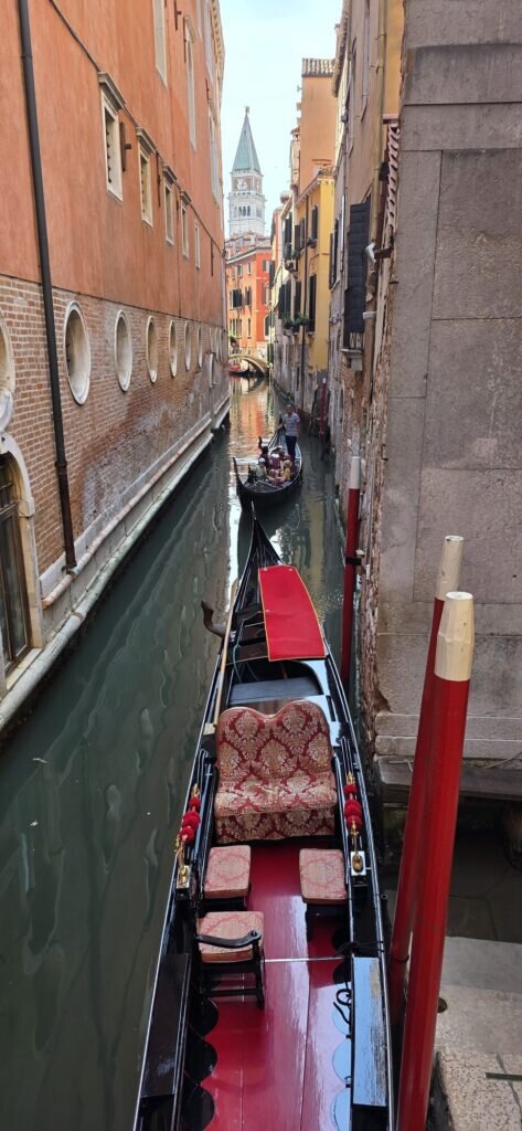 A gondola with ornate red seating gliding down a quiet Venetian canal near Rialto at dawn