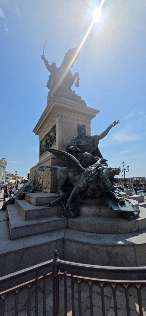 A bronze monument with a winged lion and an angel figure at the entrance to the Arsenale district