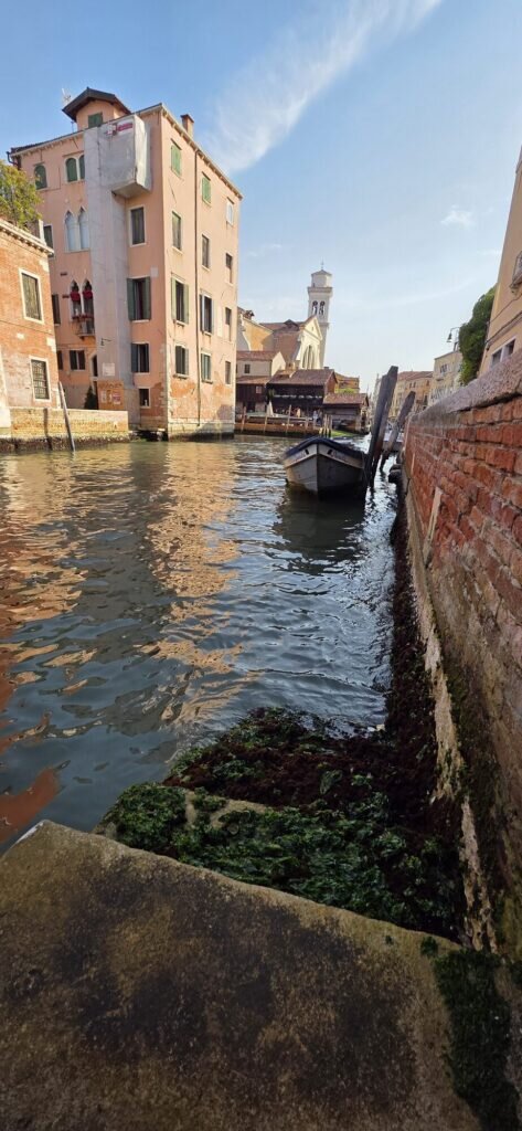 A quiet Venetian side canal at first light, moored boat and a leaning bell tower