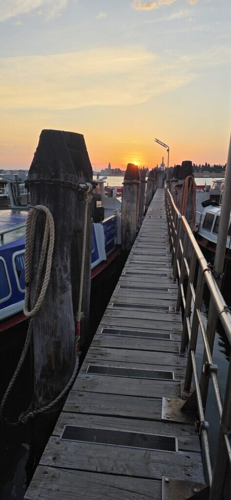 Sunrise over the Venetian lagoon seen down a wooden jetty with moored boats and coiled ropes