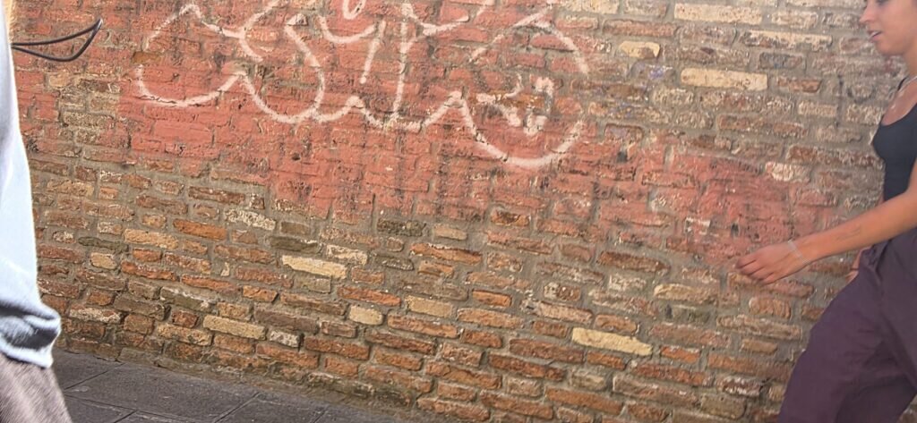 A hand resting on an old brick wall with faded chalk graffiti hearts, in late afternoon light