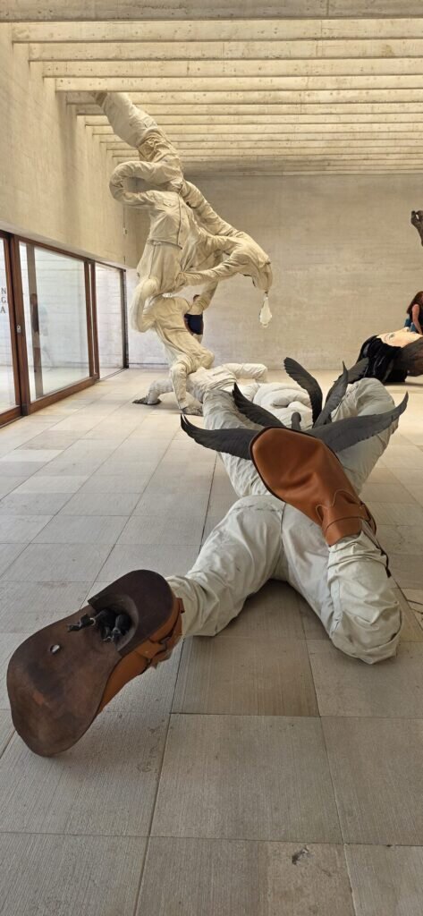 Life size canvas and feather figures with worn boots, arranged in a stone colonnade