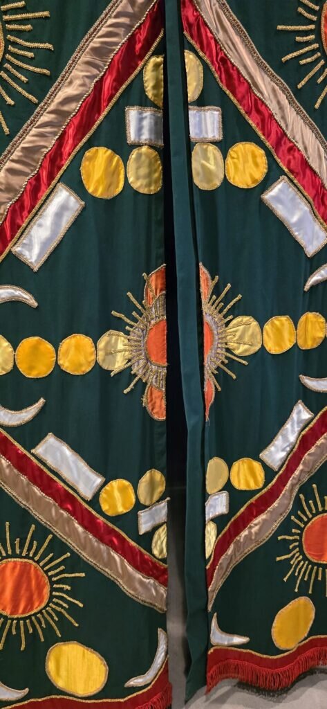 A green, gold and red embroidered textile banner with sun and moon motifs