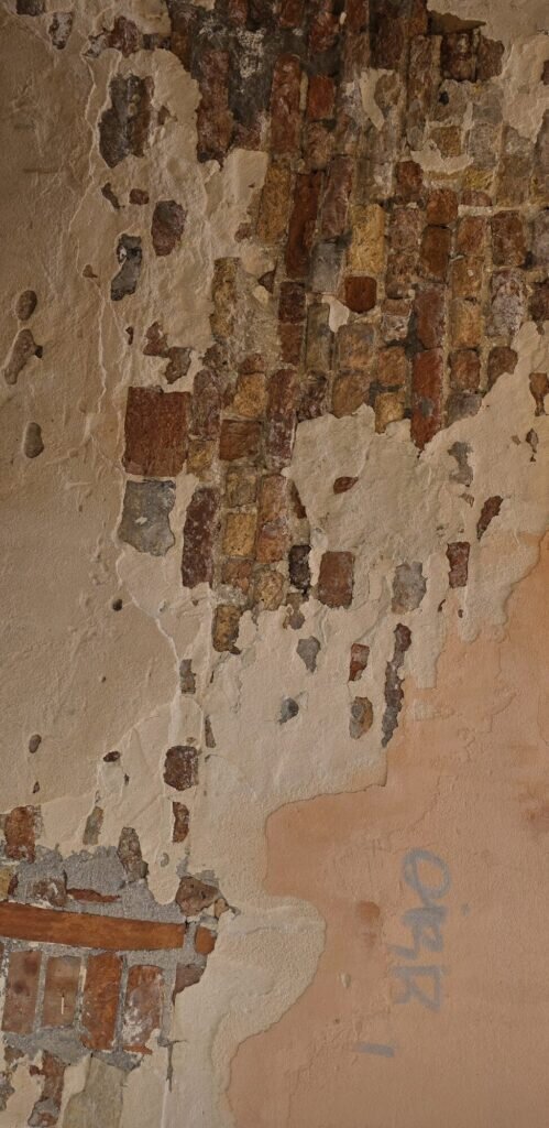 A weathered Venetian wall of peeling plaster and exposed brick in raking afternoon light