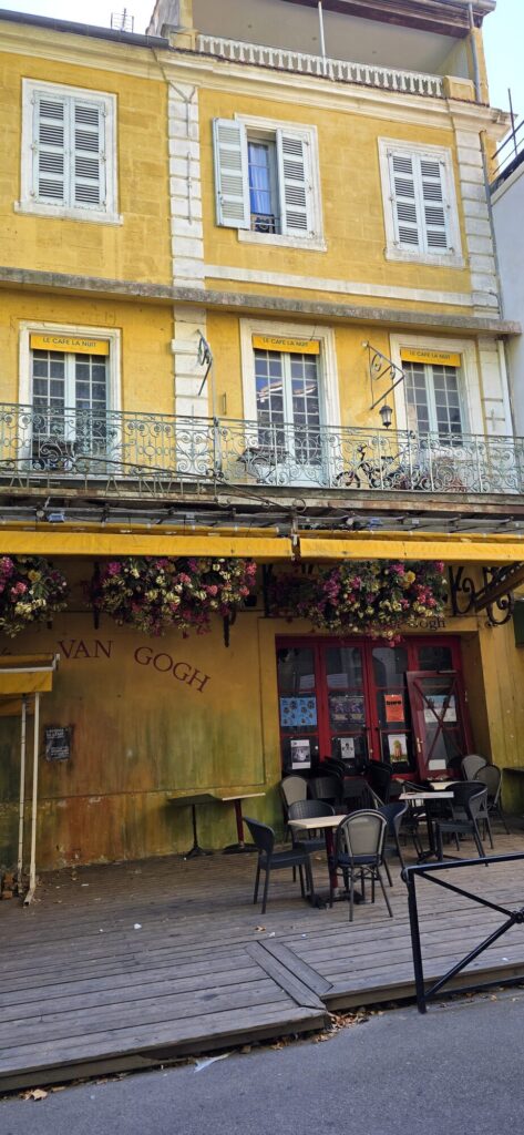 The closed yellow Cafe la Nuit on Place du Forum in Arles, chairs stacked on the terrace, dead flowers over the awning and Van Gogh painted on the wall