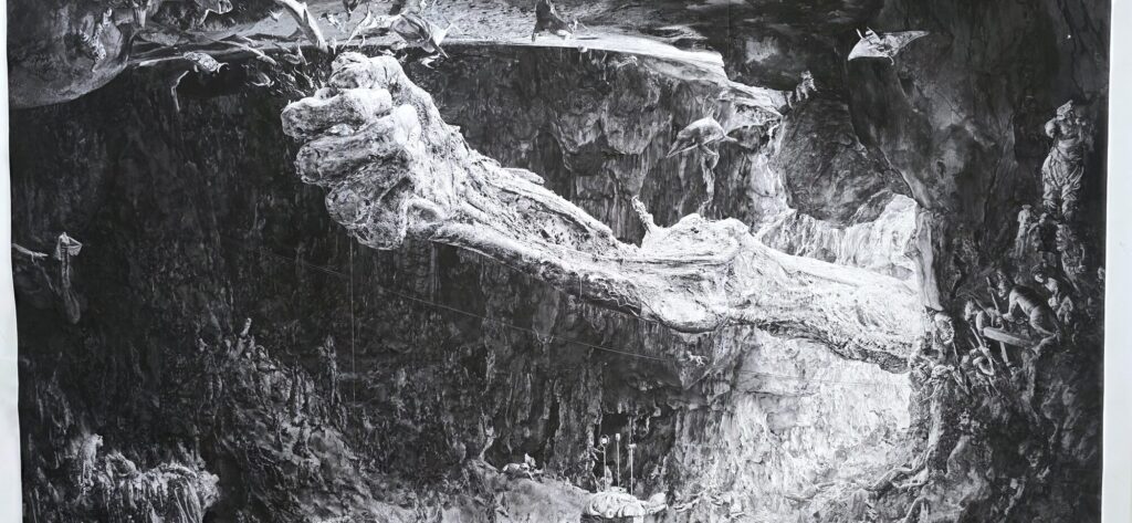 Large black and white photograph of a vast dark cliff face with a pale white formation across the middle resembling an enormous bone or limb, and small scattered white marks across the rock
