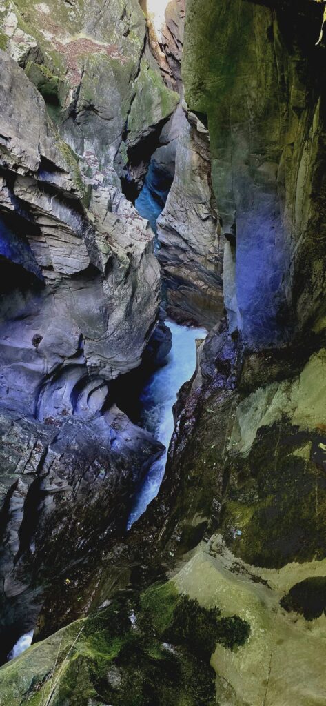 Deep inside a narrow limestone gorge, the rock carved into smooth folds and hollows in grey, gold and purple, with a thin channel of pale water running far below