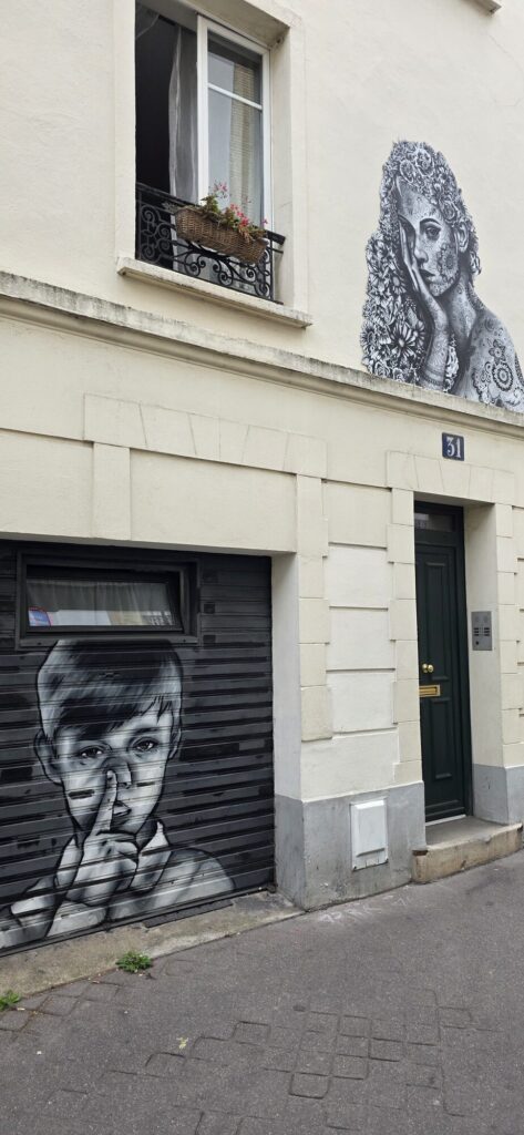 Cream facade of number 31 rue des Cinq Diamants with a black and white paste-up by Aydar of a woman made of flowers in the upper corner, and a painted portrait of a pensive face on the dark shutter below