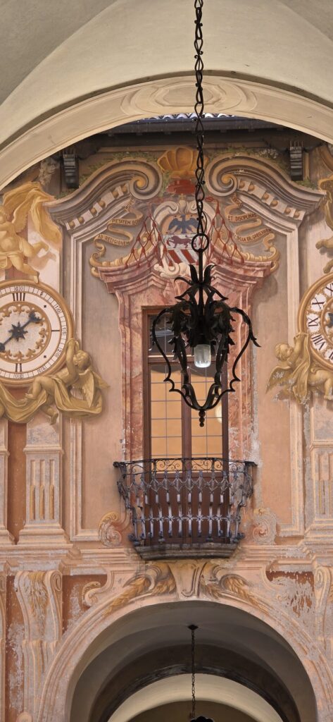 A vaulted archway painted with faded pink and ochre decoration, a wrought iron lantern hanging from a chain at its centre, and a small balcony with an iron rail set into the wall above