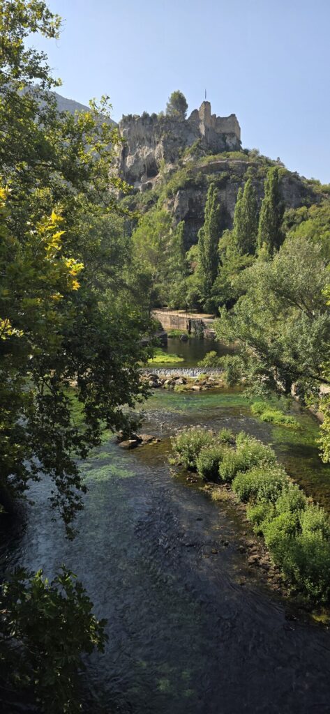 The Sorgue running clear between wooded banks and poplars, with a ruined stone castle standing on a limestone crag high above the valley