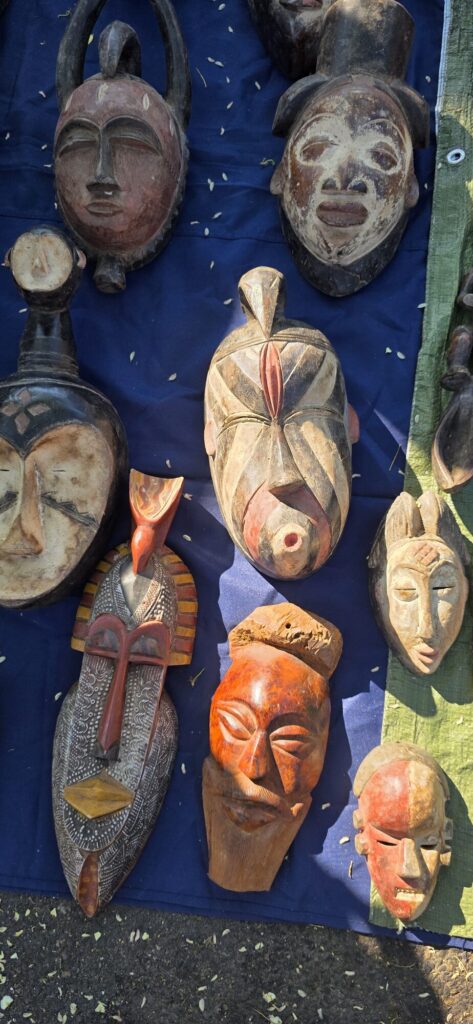 African carved wooden masks in white, red and ochre laid out on a blue tarpaulin on the ground at the Sunday market