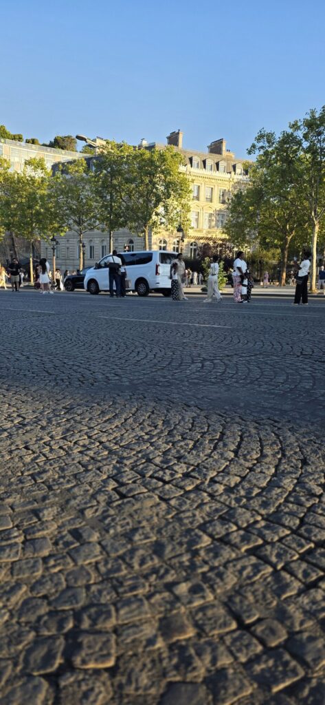 Wide sweep of cobblestones on the avenue glowing gold in the low evening sun with small distant figures and long shadows