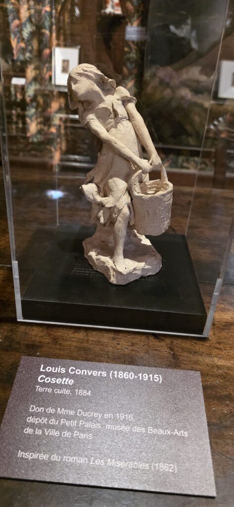 Terracotta sculpture of Cosette by Louis Convers from 1884, a young girl in a ragged dress, displayed with its museum label