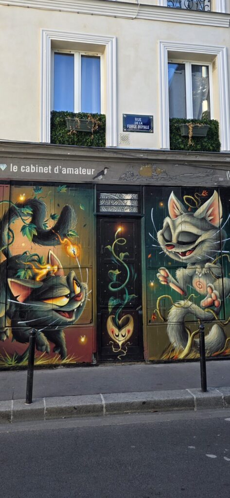 Painted mural of cats covering a wall at the corner shop le cabinet d'amateur on Rue de la Forge Royale, cats in many colours and poses across the shopfront