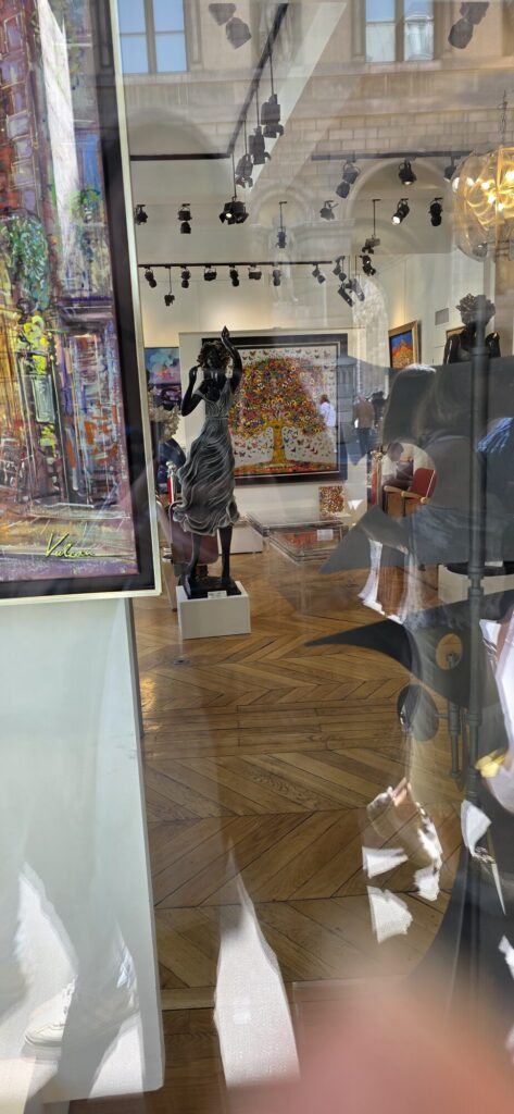 Gallery window near the Palais Royal seen through reflections, with a bronze figure sculpture, a colourful tree of life painting and a Paris street scene signed Vulcain standing on the parquet floor