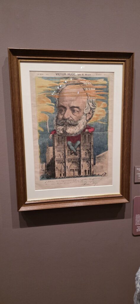 Framed caricature by H. Meyer from Le Geant showing Victor Hugo's giant head atop a tower of Notre-Dame holding a quill