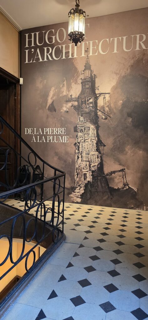 Stairwell of the Maison de Victor Hugo with the exhibition banner for Hugo et l'Architecture, de la pierre a la plume, showing one of Hugo's ink drawings of a building