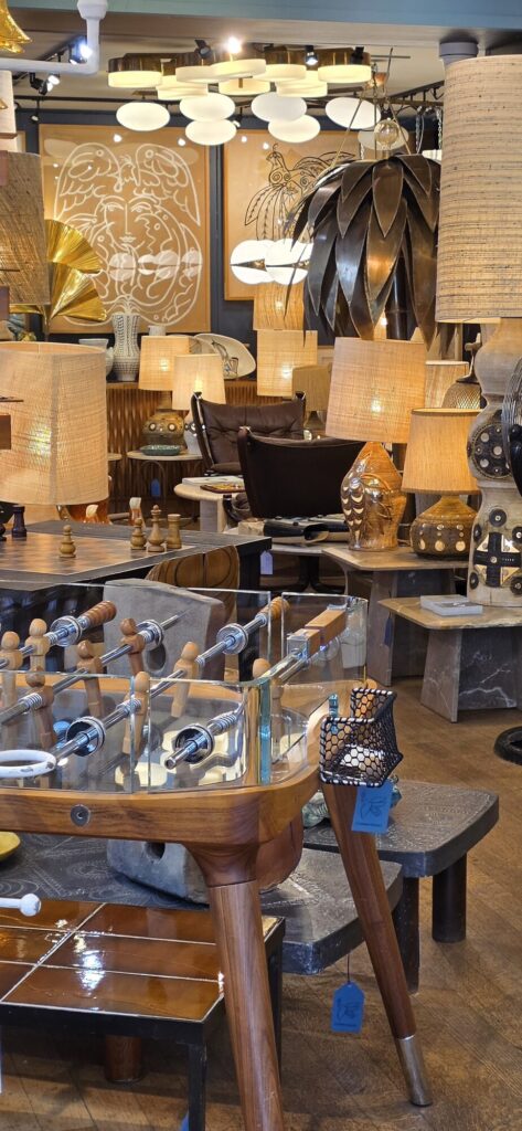 Interior of a Left Bank design shop crowded with lamps, straw shades and a vintage wooden table football in the foreground
