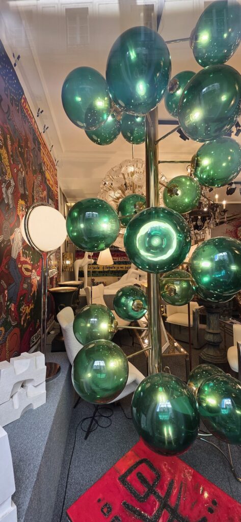 Design gallery window with a chrome stand holding dozens of green glass bubble spheres, each reflecting the street outside