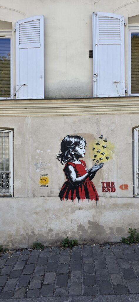 Stencil of a small girl in a black and red dress cupping her hands under a swarm of yellow and black bees painted on a pale wall, the words THE END stencilled in red beside her, white shutters above