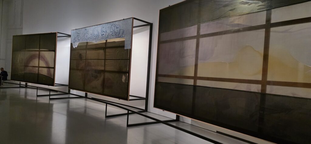 Row of very large translucent Sigmar Polke panels in metal frames standing free on a polished gallery floor, dark olive and amber washes showing through the layers